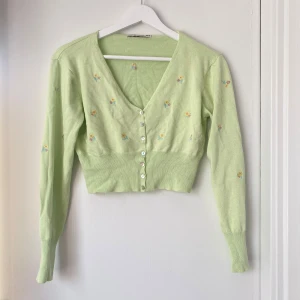Ljusgrön kofta med blommönster från BBWM - Säljer en superfin ljusgrön kofta från BBWM med söta små blommor i gult och rosa. Den är croppad och har en v-ringad design med knappar framtill. Perfekt för vår och sommar! 🌸