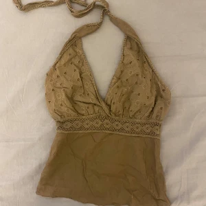 Brun halterneck topp - Säljer en snygg brun halterneck topp med spetsdetaljer. Toppen är i bomull och elastan, vilket gör den bekväm och stretchig. Perfekt för sommardagar eller en avslappnad festkväll. Tillverkad i Italien.