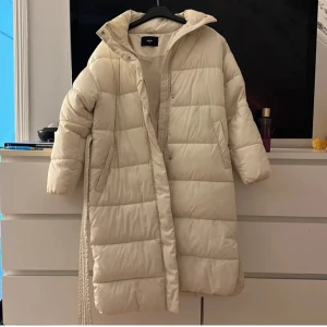 Beige lång dunjacka - Säljer en supermysig beige lång dunjacka i mycket bra skick. Perfekt för kalla vinterdagar med sin quiltade design och långa ärmar. Jackan har en dragkedja framtill och en hög krage för extra värme. Den är både stilren och praktisk, idealisk för vinterns alla äventyr! 🧥❄️