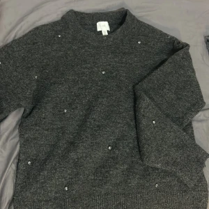 Mörkgrå stickad tröja med pärlor - Säljer en superfin mörkgrå stickad tröja från H&M. Den har långa ärmar och är dekorerad med små pärlor som ger en extra touch. Perfekt för både vardag och fest! 🖤Är i helt nytt skick, bara testad.