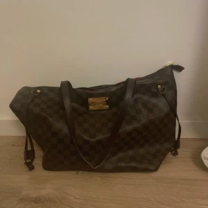 Weekend bag - Säljer en snygg brun rutig väska. Väskan har ett klassiskt rutmönster och är i mycket bra skick. Den har bruna handtag och en dragkedja upptill. Insidan är röd med mönster och har en praktisk ficka. Perfekt för både vardag och resa! Kom med prisförslag!