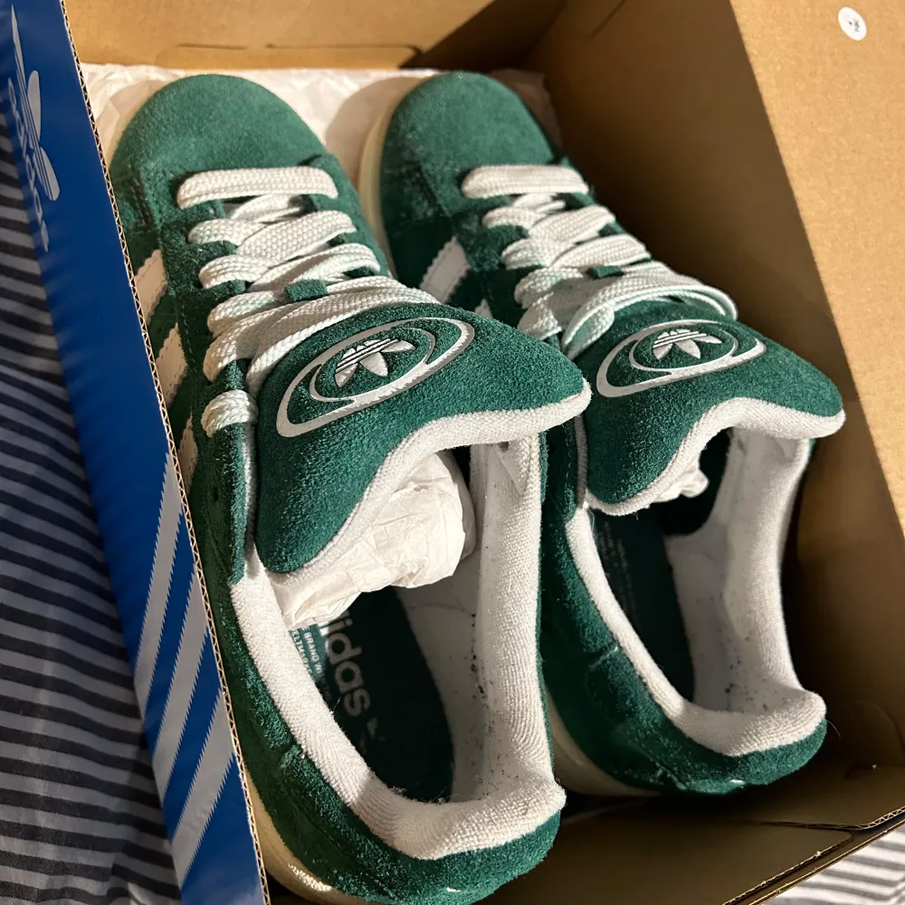 Säljer ett par snygga gröna Adidas Campus sneakers i mocka. De har de klassiska vita ränderna och en vit sula. Skorna är i bra skick, använda fåtal gånger. De kommer med extra gröna skosnören. . Skor.