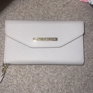 Beige plånbok från Ideal of Sweden - Säljer en stilren beige plånbok från Ideal of Sweden. Den har en praktisk dragkedja och flera kortfack inuti. Perfekt för att hålla ordning på dina kort och kontanter. Plånboken är i mycket bra skick och passar till alla tillfällen. En snygg accessoar som är både funktionell och elegant. Storlek X