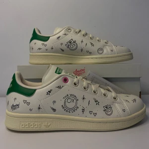 Adidas Stan Smith - Säljer ett par Adidas Stan Smith sneakers i vitt med gröna detaljer. Skorna har ett coolt och unikt mönster med små teckningar och text. Perfekt för dig som vill sticka ut! De är i nytt skick och kommer med originalförpackning.