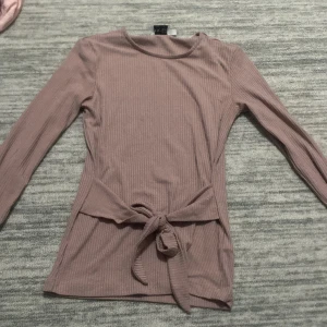 Ribbad lila tröja från NA-KD - Säljer en superfin ribbad lila tröja från NA-KD i storlek S. Den har långa ärmar och ett snyggt knytband i midjan som ger en fin passform. Perfekt för både vardag och fest! 💜