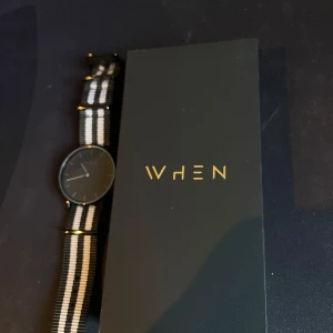 Svart och vit randig klocka från WHEN - Snygg klocka från WHEN med minimalistisk design. Den har en svart urtavla och ett randigt armband i svart och vitt. Perfekt för en stilren look. Klockan levereras i en elegant förpackning.