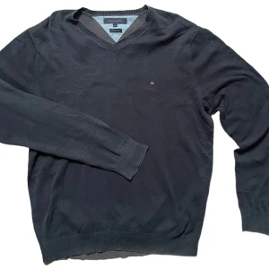 tröja från Tommy Hilfiger - Säljer en stilren tröja från Tommy Hilfiger i premium bomull. Tröjan har en v-ringad hals och långa ärmar med ribbade muddar. Perfekt för en klassisk och avslappnad look.