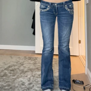 Blå jeans med detaljer - Snygga blå lågmidjade bootcut jeans från Miss Me. De är uupsprätta nedtill och mått finns på bilderna. Skriv för fler frågor.🥰