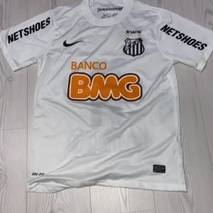 Vit fotbollströja från Nike med S.F.C. emblem - Vit kortärmad fotbollströja från Nike med S.F.C. emblem och sponsorer som BMG och Netshoes. Tröjan har nummer 11 och namn på baksidan. Perfekt för fotbollsfans!