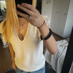 Vit blus med volangärmar från Vero Moda - Säljer en stilren vit blus från Vero Moda med v-ringning och volangdetaljer på ärmarna. Perfekt för en chic och elegant look. Blusen är i ett lätt och luftigt material.