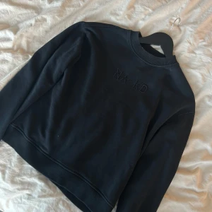Svart sweatshirt från NA-KD - Säljer en stilren svart sweatshirt från NA-KD med broderad logga på bröstet. Tröjan har långa ärmar och ribbad krage samt muddar. Perfekt för en avslappnad look.