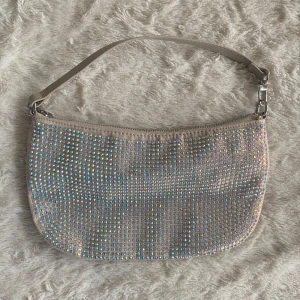 Glittrig axelväska med paljetter - Säljer en snygg glittrig axelväska täckt med skimrande paljetter. Väskan har en dragkedja upptill och en avtagbar axelrem i beige. Perfekt för att ge lite extra bling till din outfit! ✨ 