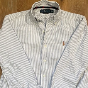 Randig blå och vit skjorta från Ralph Lauren - Modellen är 171 cm och 65 kg och tröjan sitter lite för stort. Passar dig runt 180cm. Priset är diskuterbart!