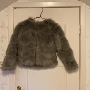 Grå pälsjacka från H&M - Säljer en snygg grå pälsjacka från H&M. Jackan har en fluffig och mjuk textur som ger en lyxig känsla. Perfekt för att hålla sig varm och stilren under kyliga dagar. Den har en enkel design utan krage och är lätt att matcha med olika outfits.😻
