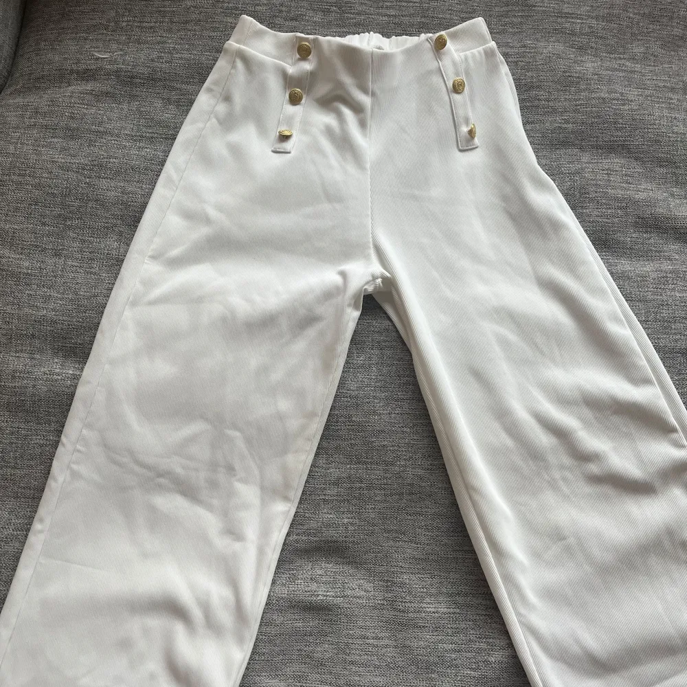 Snygga vita byxor från Zara med hög midja och dekorativa knappar framtill. Byxorna har en loose passform och är perfekta för en stilren look. Tillverkade i ett mjukt och bekvämt material. Aldrig andvända!. Farkut & Housut.