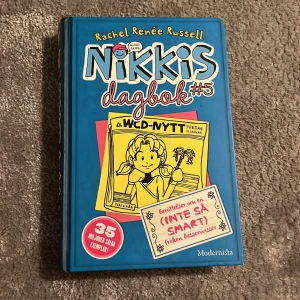 Nikkis dagbok #5 - Säljer boken 'Nikkis dagbok #5' av Rachel Renée Russell. Den har en blå omslag med illustrationer och text i olika färger. Boken är en del av en populär serie med humoristiska berättelser om Nikki och hennes äventyr. Perfekt för ungdomar som gillar dagboksstil och roliga historier.