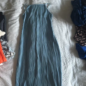 Blå ribbad klänning - Snygg blå klänning med ribbad struktur och smala axelband. Perfekt för en stilren look. Klänningen har en lång passform som ger en elegant siluett.