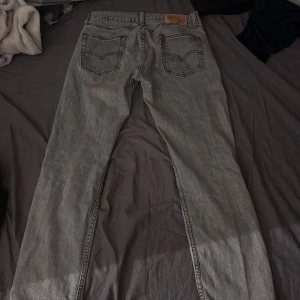 Grå jeans Levi's - Säljer ett par grå jeans från Levi’s, riktig snygga och skicket är bra förutom att levi’s lappen (den bruna) har spruckit men inget som synt när man har bälte på sig eller bara en tröja som går över det.