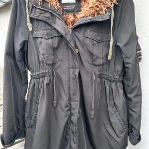 Svart parkas från Odd Molly! - Svart parkas med fickor fram, knappar, dragkedja, dragsko i midjan, luvan och mjuk fuskpäls i storlek L från Odd Molly. Sparsamt använd och hel och ren.