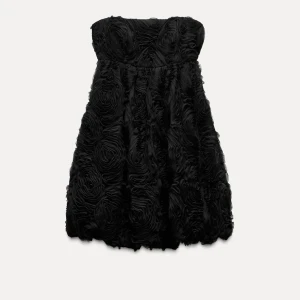 Svart Zara klänning - Elegant svart axelbandslös klänning från Zara med vackra rosdetaljer i tyget. Perfekt för en festlig kväll. Tyvärr inte så bra egna bilder men har endast testat på klänningen och lappen sitter fortfarande kvar!