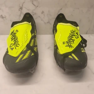 Svarta och gula fotbollsskor från Adidas - Snygga Adidas Predator fotbollsskor i svart och neon-gult med unika grafiska detaljer. Skorna har en strömlinjeformad design med dobbar för optimalt grepp på planen. Perfekta för den som vill sticka ut på fotbollsplanen. Priset är inte hugget i sten!!!!!