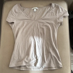 Beige t-shirt från H&M - Säljer en stilren beige t-shirt från H&M. Den har en v-ringad design och korta ärmar, perfekt för en avslappnad look. Gjord i mjukt material för extra komfort. Storlek L men passar även en M