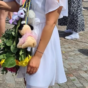 Vit klänning med knytband - Elegant vit klänning med v-ringning och knytband i midjan. Klänningen har korta ärmar med volangdetaljer och en luftig design som passar perfekt för sommarens festligheter.