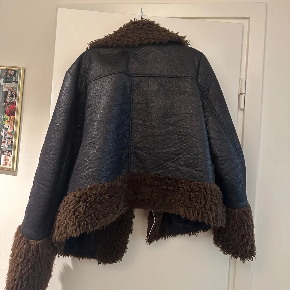 Snygg svart skinnjacka från Ivyrevel med mjuka bruna pälsdetaljer på krage, ärmslut och nederkant. Jackan har en cool asymmetrisk dragkedja och två praktiska fickor med dragkedjor. Perfekt för att hålla stilen i kyligare väder.. Takit.
