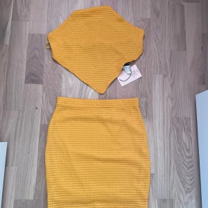 Gul kjol med matchande topp - Snygg gul kjol med matchande topp i ett stickat material. Kjolen har en tight passform och är perfekt för sommarens varma dagar. Toppen är en tubtopp som knyts i ryggen för en justerbar passform. Ett set som verkligen sticker ut i mängden!