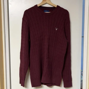 Vinröd stickad tröja från Gant - Snygg vinröd stickad tröja från Gant med kabelstickat mönster. Tröjan har en rund halsringning och långa ärmar. Perfekt för kyligare dagar och ger en stilren look.