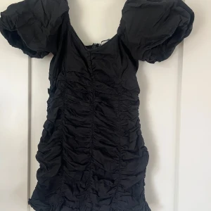 Svart klänning från Gina Tricot - Snygg svart klänning från Gina Tricot med puffiga kortärmar och rynkade detaljer. Perfekt för en stilren look. Klänningen har en dragkedja i ryggen för enkel påklädning.