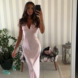 Balklänning - Elegant ljusrosa långklänning med v-ringad design och ärmlös stil. Perfekt för speciella tillfällen med sin mjuka och flytande passform.