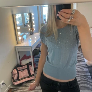 Grå topp med pärlor - Säljer en blå topp med pärlor. Toppen har en ribbad nederkant som ger en snygg passform. Perfekt till våren!