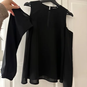 Svart blus från by Me - Snygg svart blus från by Me med offshoulder-design och långa ärmar. Perfekt för en stilren look.