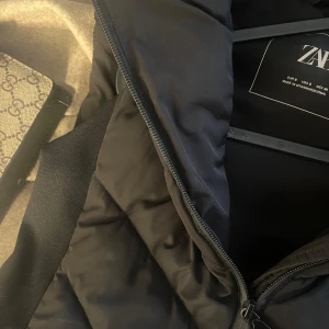 Svart dunväst med huva - Säljer denna populära västen. Svårt att få tag på nu. Sitter jättefint i midjan. Säljer den för att jag inte fick mycket användning av den, endast en gång.