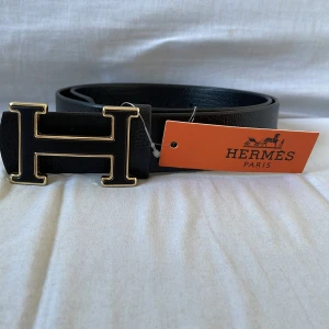 Svart bälte med svartguldig logga - Jag säljer ett svart bälte med svartguldig logga. Bältet är snyggt och passar till olika stilar. Det är aldrig använt och är i nytt skick. Pris kan diskuteras vid snabb affär.