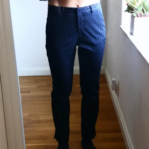 Mörkblå byxor med diskret mönster - Mörkblå byxor med ett diskret geometriskt mönster. De är perfekta för en stilren look. Byxorna har hällor för bälte och en klassisk design med dragkedja framtill. Från Stockholm 