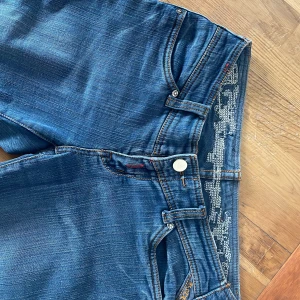 Blå jeans från Miss ViVi Jeans - Snygga blå jeans från Miss ViVi Jeans med dekorativa detaljer på bakfickorna och midjebandet. De har en klassisk femficksdesign och en knappgylf. Perfekta för en stilren look.