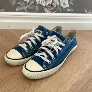 Blå sneakers från Converse - Säljer ett par klassiska blå Converse sneakers med vit sula och snörning. Skorna är i bra skick och har inte använts så mycket. Perfekta för en avslappnad stil. Hör gärna av er för fler frågor eller funderingar😇