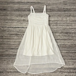 Vit klänning med smala axelband - Säljer en elegant vit klänning med smala axelband och en luftig kjol. Klänningen har en vacker rynkad detalj på överdelen och en asymmetrisk nederdel som ger en fin siluett. Perfekt för sommarens alla tillfällen!🌺