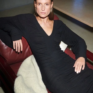 Malene Birger Delisa dress   - Elegant svart långklänning med v-ringning och långa ärmar. Klänningen har en åtsittande passform och är tillverkad i ett stretchigt material som ger en smickrande silhuett. Perfekt för en stilren look.