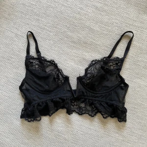 Svart spets bralette/bh från NLY Lingerie - Snygg svart spets bralette med volangdetaljer. Den har justerbara axelband och en vacker spetsdesign. 