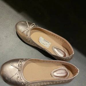GuldRosa ballerinaskor med rosett - Säljer helt nya ballerina skor från Copenhagen|kids. Snygga rosa ballerinaskor i lädermaterial med dekorativ rosett på tån. Skorna har ett fint perforerat mönster längs kanterna som ger en elegant touch. Perfekta för en stilren look.