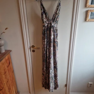 Mönstrad långklänning med v-ringning - Säljer en vacker långklänning med ett färgglatt mönster i olika nyanser. Klänningen har en djup v-ringning och smala axelband, vilket ger en elegant look. Perfekt för sommarens alla tillfällen. 🌸