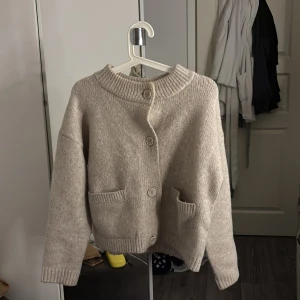Beige stickad kofta med knappar - Mysig beige stickad kofta. Ribbade detaljer på fickorna, armarna och kragen. Jätte fint skick, endast använd ett fåtal gånger. De står att storleken är XXS men den passar även xs och s.  