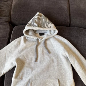 Grå syna world Hoodie - Säljer nu min helt nya syna world hoodie den är helt ny med inga skador och helt oanvänd gillar inte riktigt hur den satt den är en storlek L men sitter som M pris går att diskuteras