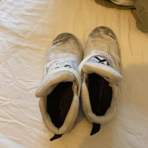 Vita innebandyskor från Unihoc - Säljer ett par vita innebandyskor från Unihoc med hög ankel och kardborreband för extra stöd. Skorna har en robust sula och är designade för målvakter. Perfekta för inomhusbruk och ger bra grepp på planen. De är använda i en halv säsong en röd fläck på sidan av vänstra skon. Kan sänka pris det är bara att kontakta hyfsat bra skick