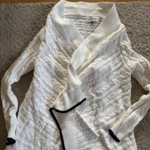 Vit stickad kofta med svarta detaljer - Säljer en vit stickad kofta med snygga svarta detaljer vid kanterna. Koftan har ett fint mönster och långa ärmar. Perfekt för kyliga dagar och ger en stilren look. Tillverkad i 100% bomull för extra komfort.