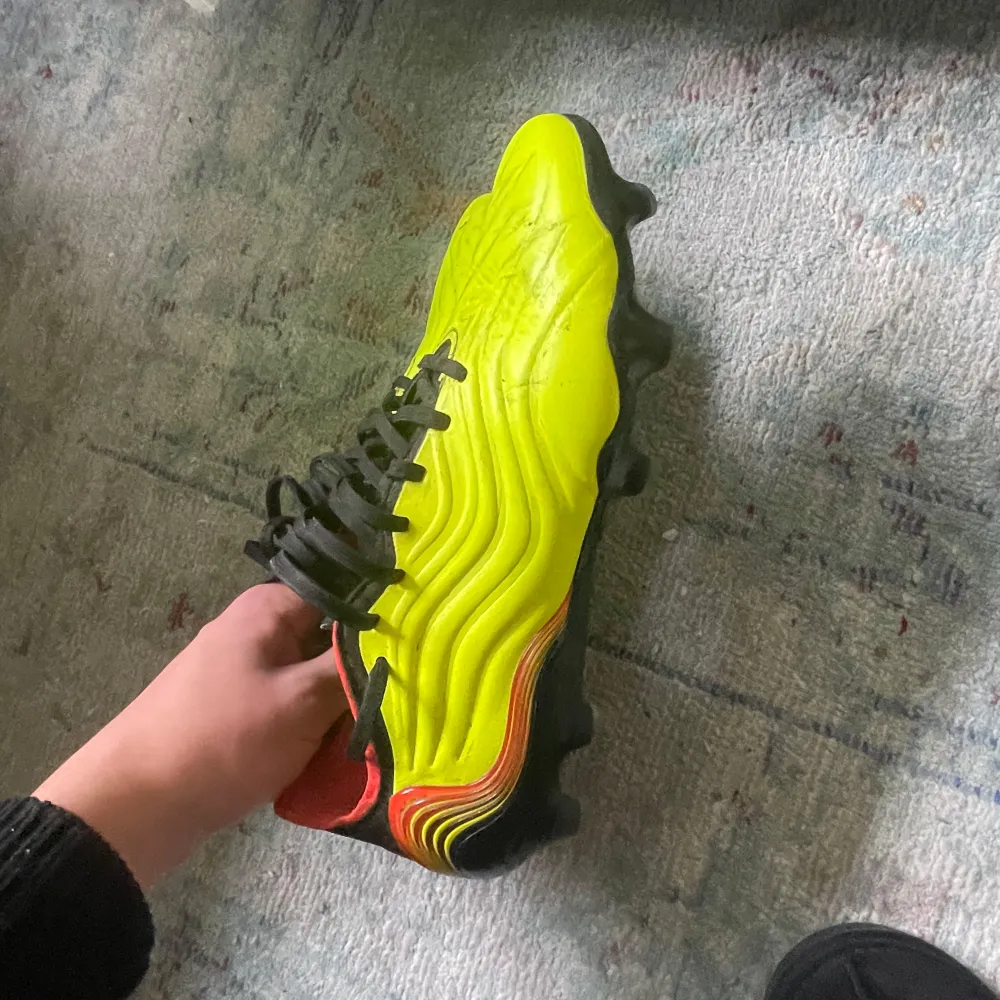 Snygga gula fotbollsskor från Adidas med svarta och röda detaljer. Perfekta för fotbollsspelare som vill sticka ut.. Kengät.