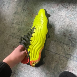 Gula fotbollsskor från Adidas - Snygga gula fotbollsskor från Adidas med svarta och röda detaljer. Perfekta för fotbollsspelare som vill sticka ut.
